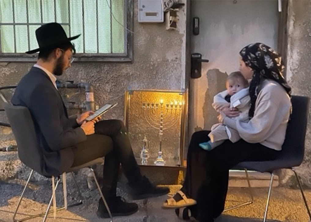 סיור חנוכיות - משפחה מקומית מדליקה חנוכיה בפתח ביתה